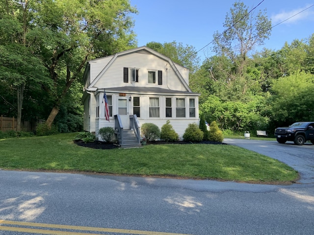 dutch colonial featuring a gambrel roof, a front lawn, and fence