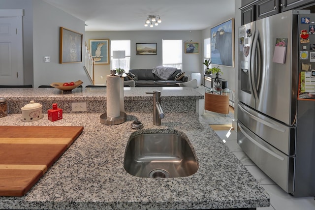 kitchen featuring stainless steel fridge with ice dispenser, light stone counters, open floor plan, and a sink