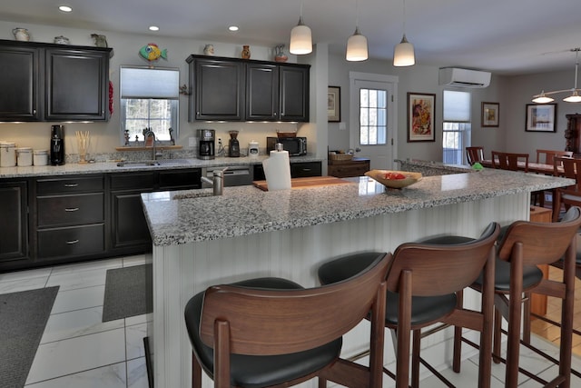 kitchen featuring a sink, decorative light fixtures, a kitchen breakfast bar, a wall unit AC, and dark cabinetry