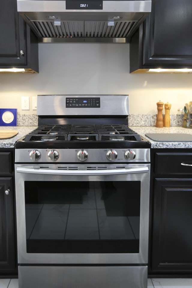 kitchen with stainless steel gas range, wall chimney range hood, and dark cabinetry