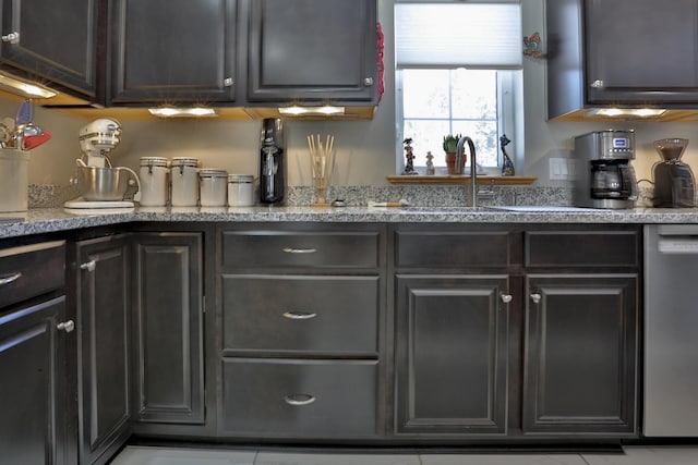 kitchen with stainless steel dishwasher, light stone counters, and a sink