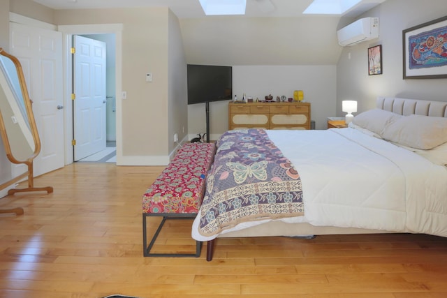 bedroom featuring vaulted ceiling with skylight, wood-type flooring, and a wall unit AC