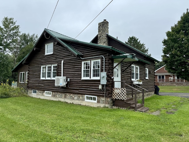 exterior space with log siding, a chimney, a yard, and ac unit