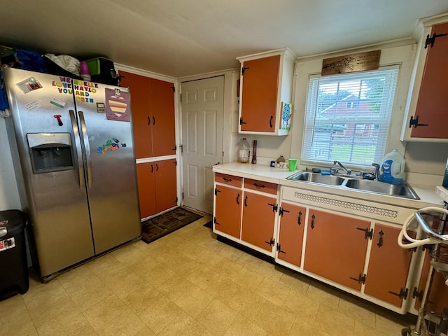 kitchen featuring crown molding, light floors, light countertops, stainless steel refrigerator with ice dispenser, and a sink