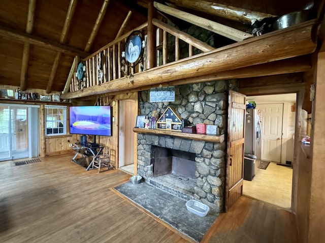 living area featuring a stone fireplace, beam ceiling, wood finished floors, and wooden ceiling