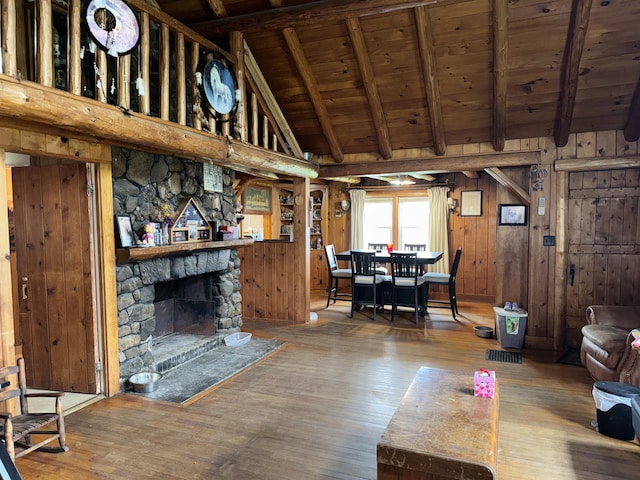 living area featuring beamed ceiling, wood walls, wooden ceiling, a fireplace, and wood finished floors