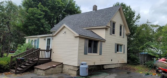 view of front facade featuring a patio, fence, a chimney, and a shingled roof