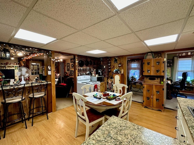 dining area with a bar, separate washer and dryer, wood finished floors, and a paneled ceiling