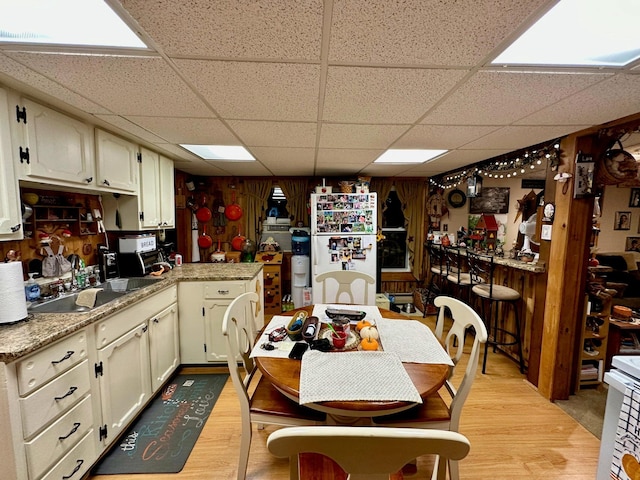 kitchen with freestanding refrigerator, a sink, light countertops, a paneled ceiling, and light wood-type flooring