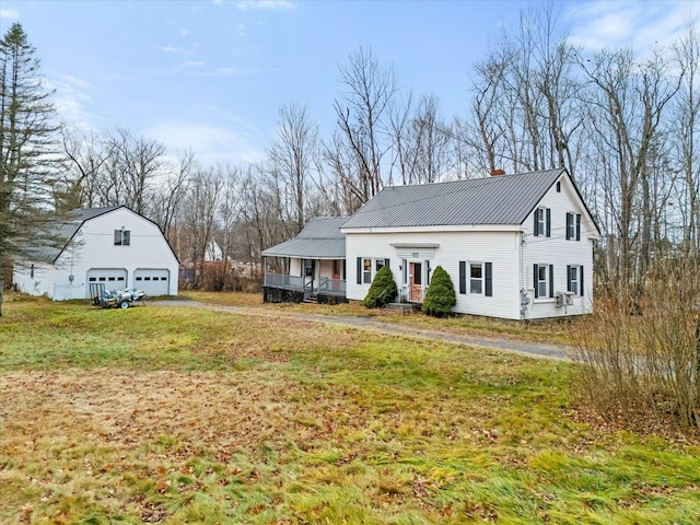 view of front of property with a front yard, a chimney, an outdoor structure, a detached garage, and metal roof