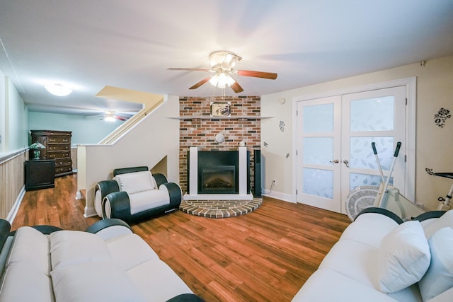 living room with a brick fireplace, wood finished floors, french doors, and ceiling fan