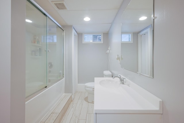 full bath with visible vents, toilet, vanity, and shower / bath combination with glass door