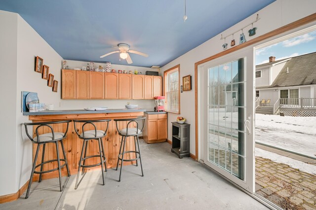 kitchen featuring a ceiling fan, baseboards, concrete floors, a peninsula, and a kitchen bar