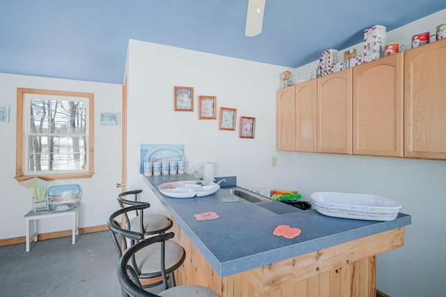 kitchen with dark countertops, light brown cabinets, baseboards, concrete flooring, and a kitchen breakfast bar