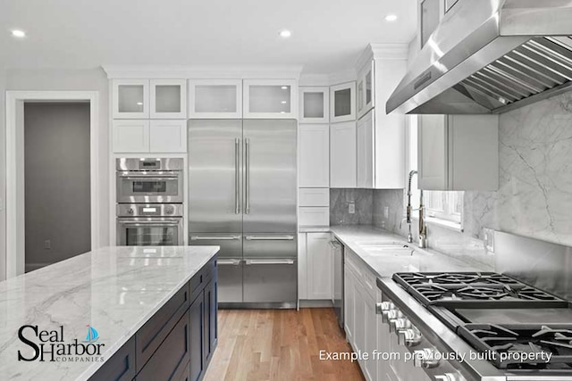 11 Clam Ln Unit A, Wells, ME 04090 - kitchen with stainless steel appliances, wall chimney exhaust hood, white cabinetry, a sink, and light stone counters