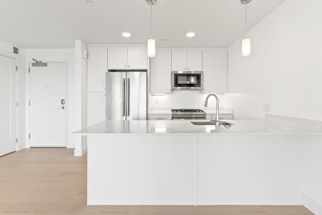 kitchen featuring light wood finished floors, a sink, appliances with stainless steel finishes, a peninsula, and light countertops