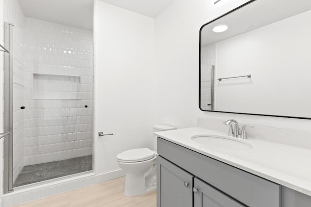 bathroom featuring wood finished floors, toilet, a stall shower, and vanity