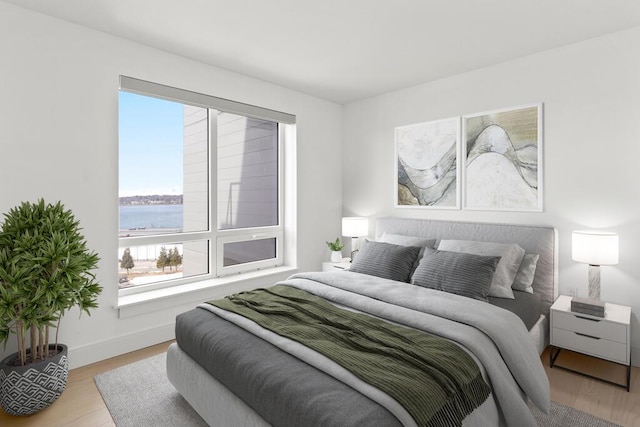 bedroom with baseboards, a water view, and wood finished floors