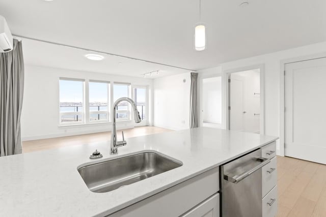 kitchen featuring light stone counters, light wood-style flooring, a sink, hanging light fixtures, and stainless steel dishwasher