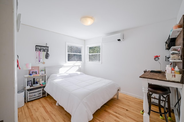 bedroom featuring light wood-style floors, baseboards, and a wall mounted air conditioner