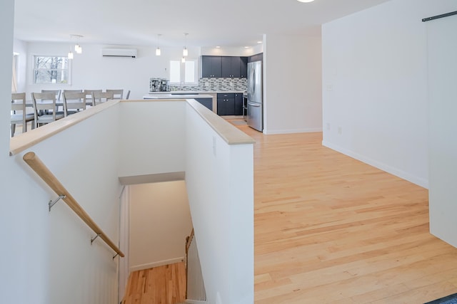 kitchen featuring decorative backsplash, light wood-style flooring, a wall mounted air conditioner, and freestanding refrigerator