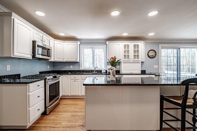 kitchen with a breakfast bar area, white cabinetry, stainless steel appliances, and dark stone countertops