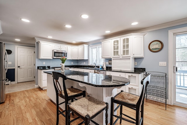 kitchen with a kitchen bar, white cabinets, ornamental molding, and stainless steel appliances