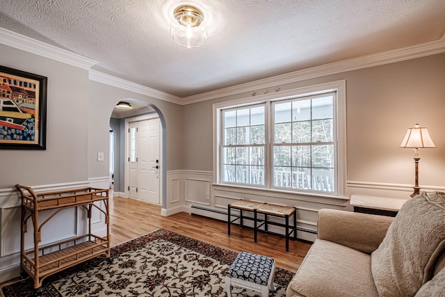 living area with a textured ceiling, wood finished floors, arched walkways, wainscoting, and a baseboard heating unit