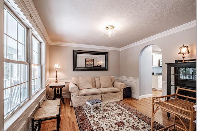 living room with crown molding, arched walkways, light wood finished floors, and a textured ceiling