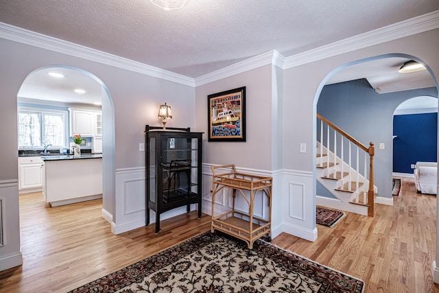 interior space featuring light wood-style flooring, arched walkways, wainscoting, stairs, and a textured ceiling