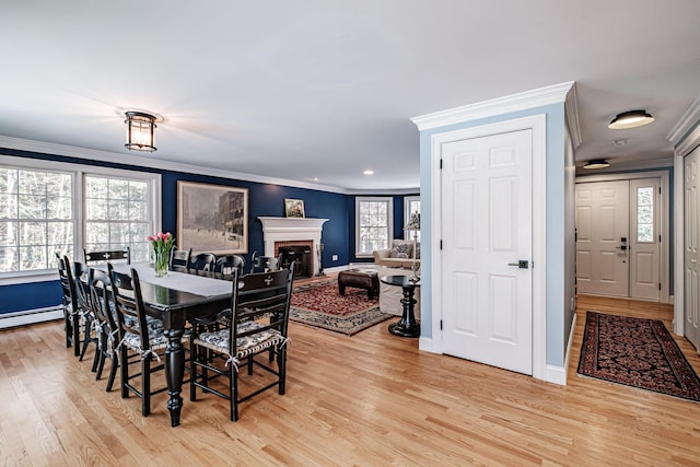 dining room with baseboards, a brick fireplace, ornamental molding, and light wood finished floors