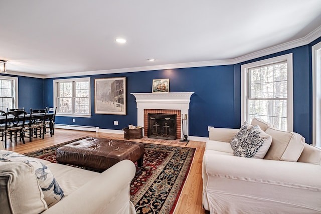 living area with a brick fireplace, a baseboard heating unit, baseboards, ornamental molding, and wood finished floors