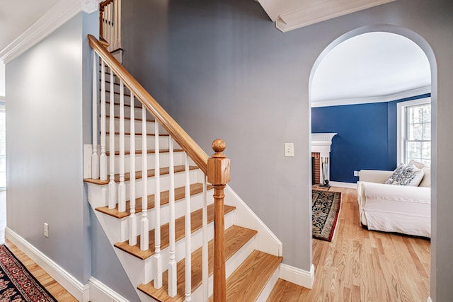 stairway with wood finished floors, baseboards, a fireplace, arched walkways, and ornamental molding