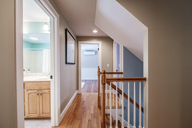 hall with a wall mounted air conditioner, an upstairs landing, light wood-style flooring, a sink, and baseboards