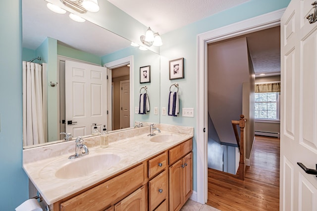 bathroom with double vanity, a baseboard radiator, wood finished floors, and a sink