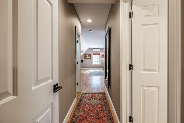 hallway with light wood-type flooring, baseboards, and vaulted ceiling