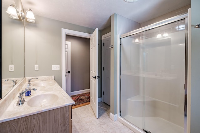 bathroom with a textured ceiling, double vanity, a stall shower, and a sink