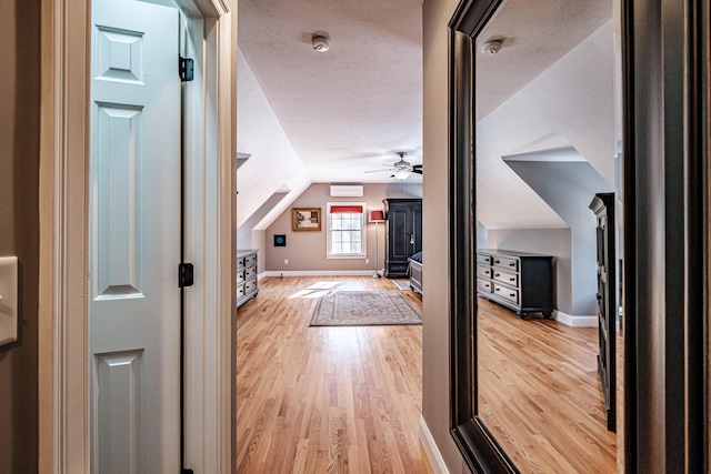 interior space with a textured ceiling, light wood-type flooring, baseboards, and vaulted ceiling