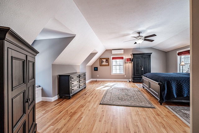 bedroom with lofted ceiling, light wood-style flooring, a wall mounted AC, a textured ceiling, and baseboards