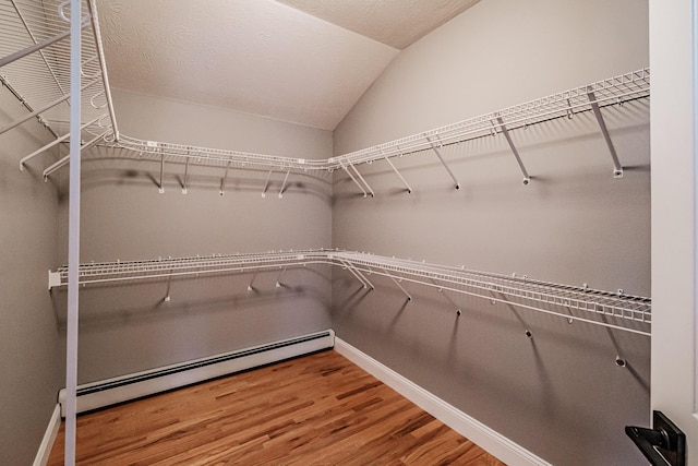 spacious closet with baseboard heating, wood finished floors, and vaulted ceiling