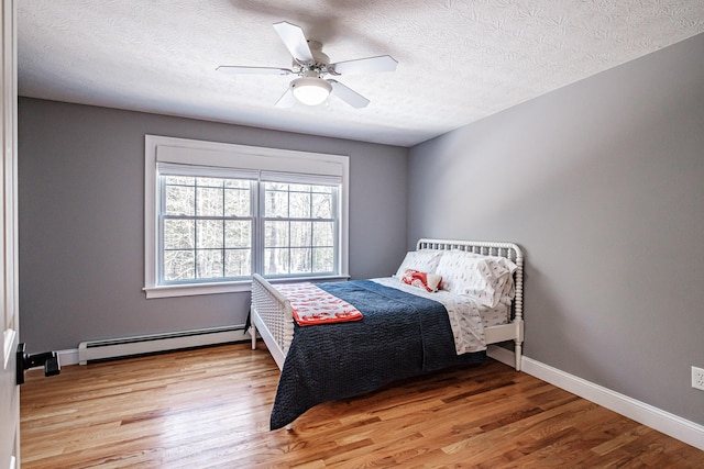 bedroom with baseboards, baseboard heating, light wood-style flooring, and a ceiling fan