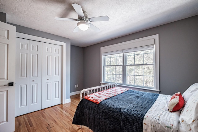 bedroom featuring a ceiling fan, a textured ceiling, a closet, light wood-style floors, and baseboards