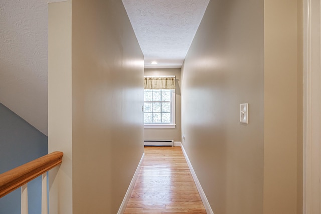 hallway featuring light wood-type flooring, a baseboard heating unit, baseboards, and a textured ceiling