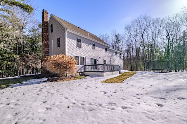 rear view of property featuring a wooden deck, a trampoline, and a chimney