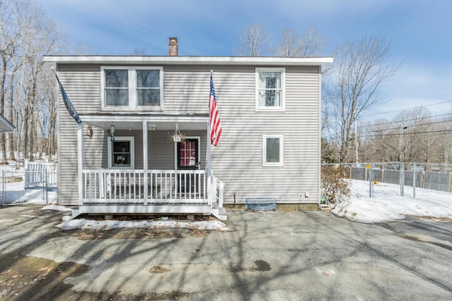 snow covered property featuring covered porch, a chimney, and fence