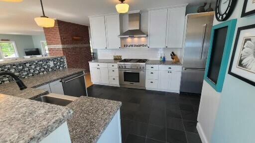 20 Wharf Rd, Blue Hill, ME 04614 - kitchen featuring wall chimney exhaust hood, appliances with stainless steel finishes, backsplash, white cabinetry, and decorative light fixtures
