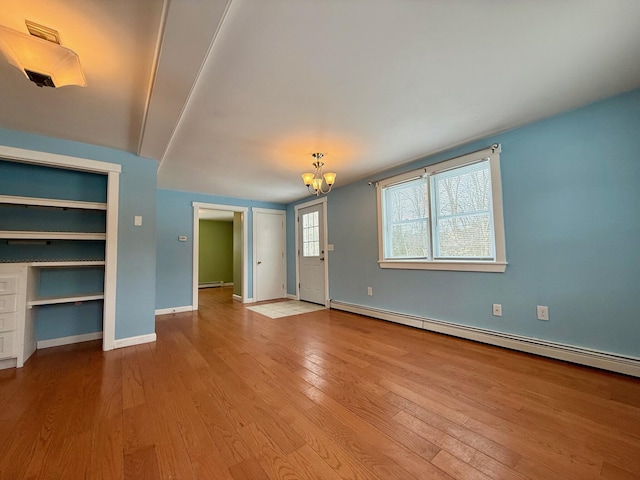 unfurnished living room with wood finished floors, visible vents, baseboards, a baseboard radiator, and a notable chandelier