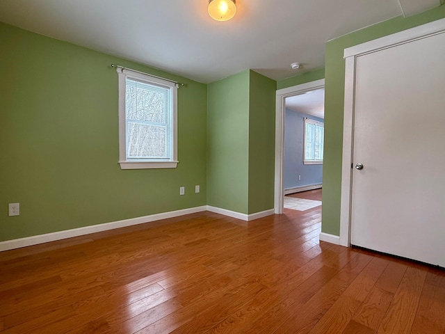 unfurnished room featuring baseboard heating, baseboards, and wood finished floors