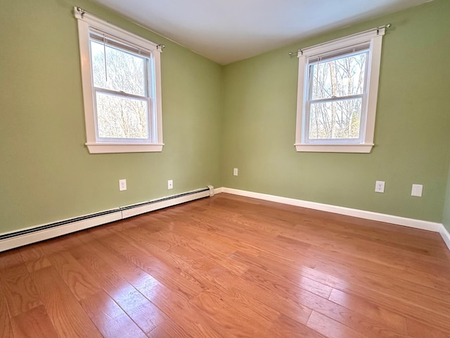 spare room with baseboards, baseboard heating, a healthy amount of sunlight, and wood finished floors