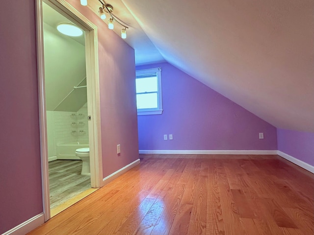 additional living space with light wood-style flooring, baseboards, and vaulted ceiling